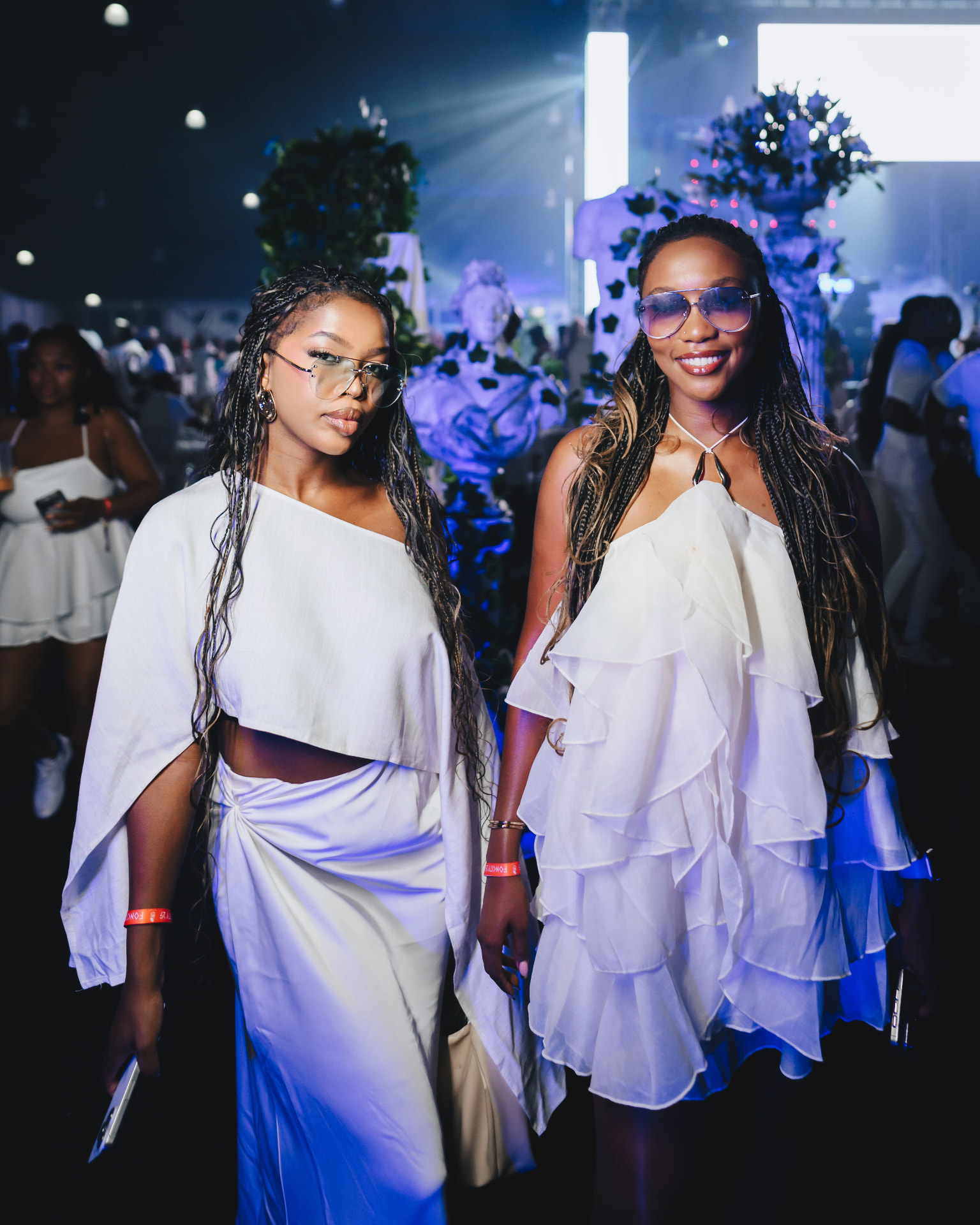 Two guests in white ruffled outfits posing under blue party lights