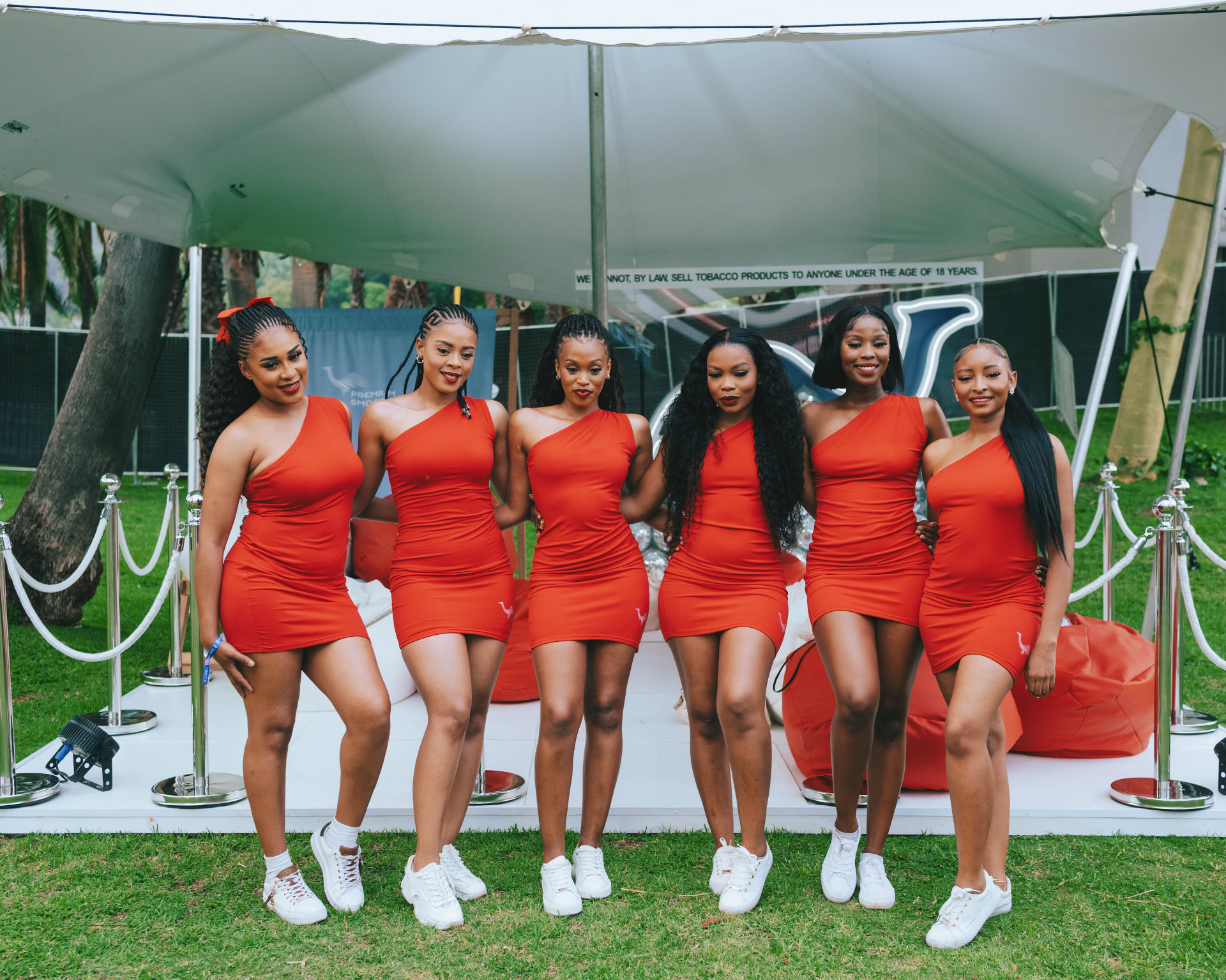 Six hosts in matching red dresses posing under a tent at the day party
