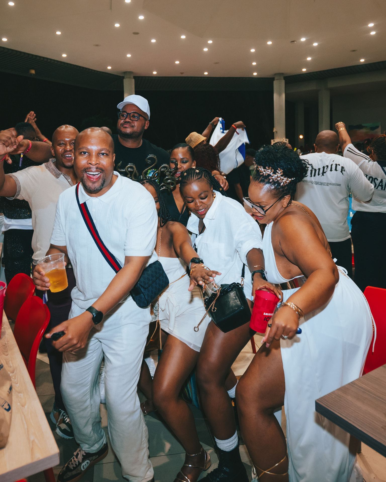 Group of guests in white outfits dancing together at the indoor party